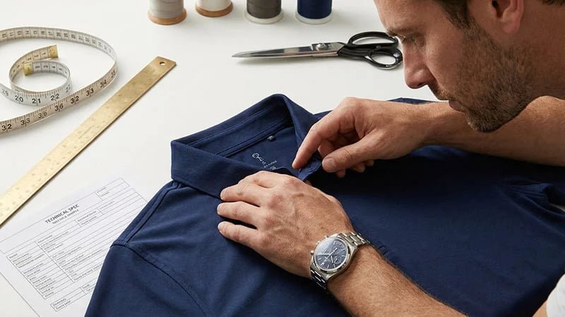 A person inspecting the collar and seams of a polo shirt sample.