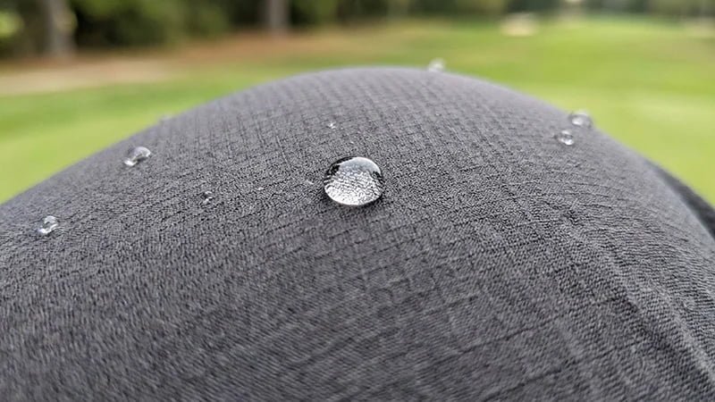 A close-up shot of a technical golf pant fabric, showing its texture and a water droplet beading on the surface