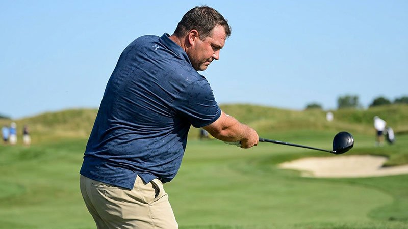 A model who wears Big & Tall sizing comfortably swinging a golf club in a well-fitting polo